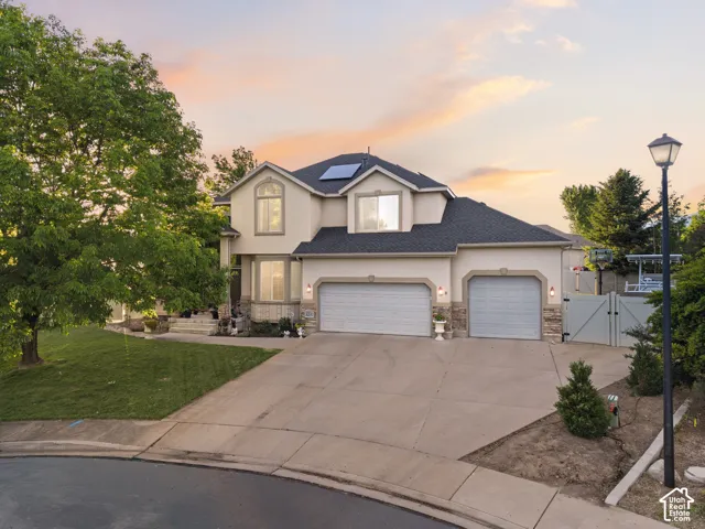 Stucco exterior with stone accents, featuring a two-car garage, solar panels, and a concrete driveway