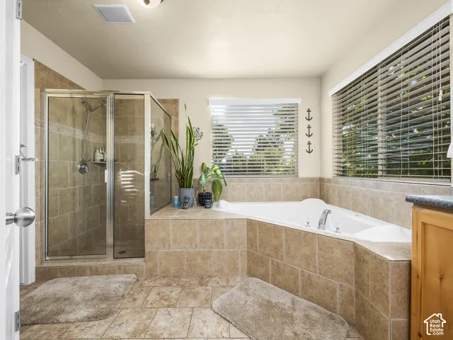 Tiled bathroom featuring a glass-enclosed shower, built-in corner soaking tub, and multiple windows with blinds