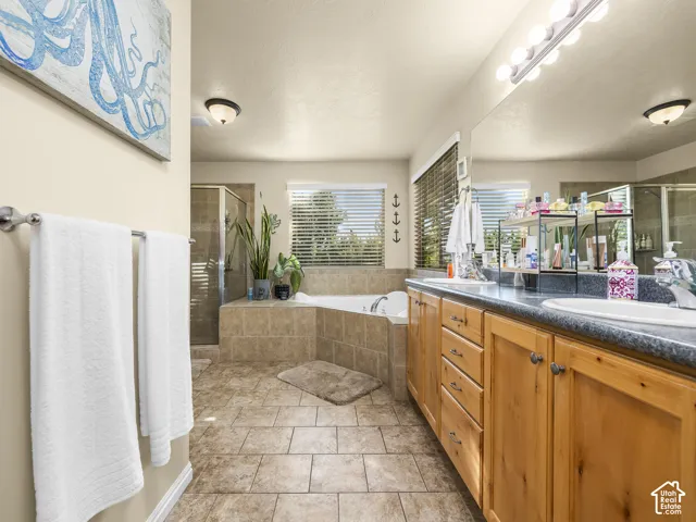 Bathroom featuring dual sink vanity with wood cabinetry, tiled flooring, built-in soaking tub, and a glass-enclosed shower