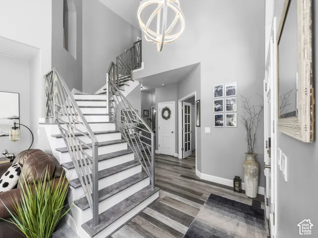 Two-story entryway featuring wood-finish flooring, a contemporary chandelier, and a white and grey staircase with metal railings