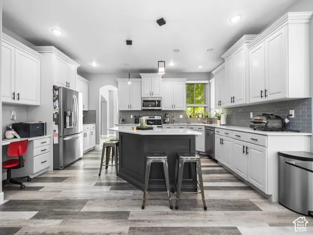 Spacious kitchen featuring an expansive center island with seating, extensive white cabinetry, stainless steel appliances, and wood-finish flooring