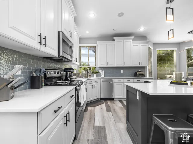 Modern kitchen featuring white shaker cabinetry with matte black hardware, stainless steel appliances, a textured blue subway tile backsplash, light-toned wood-finish flooring, and a contrasting dark gray kitchen island with a white countertop