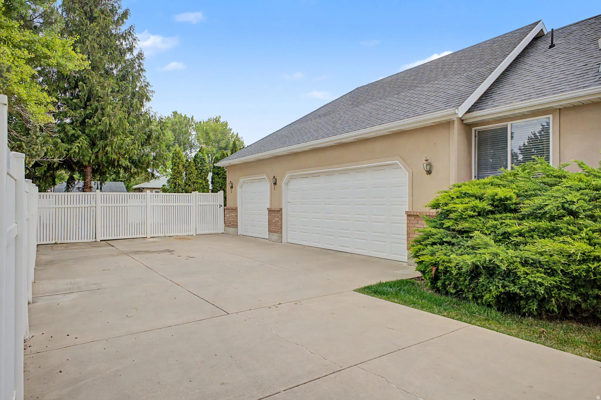 Expansive concrete driveway with a two-car garage featuring individual white doors and brick accents