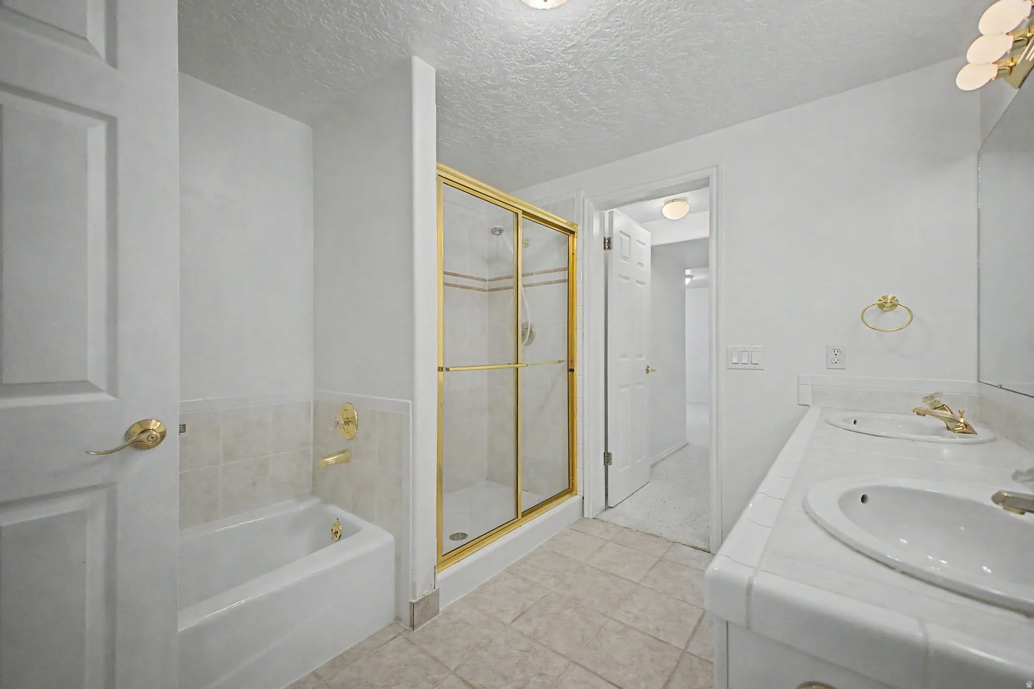 Bathroom featuring a dual vanity, gold-framed glass shower enclosure, and a built-in bathtub with tiled surround