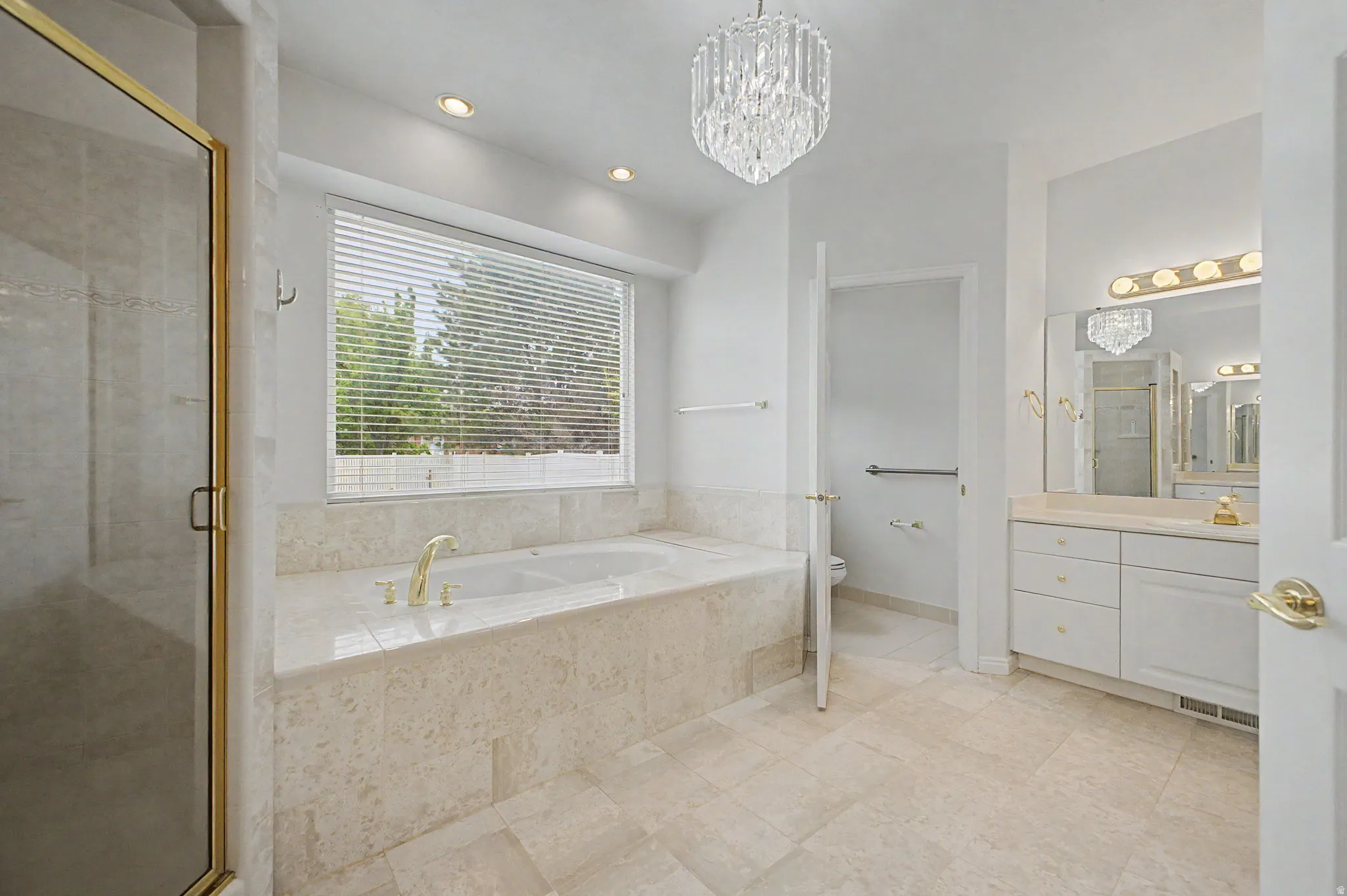 Spacious bathroom featuring a built-in soaking tub with gold-finish fixtures, a separate glass-enclosed shower with gold-finish trim, and a double vanity with a large mirror