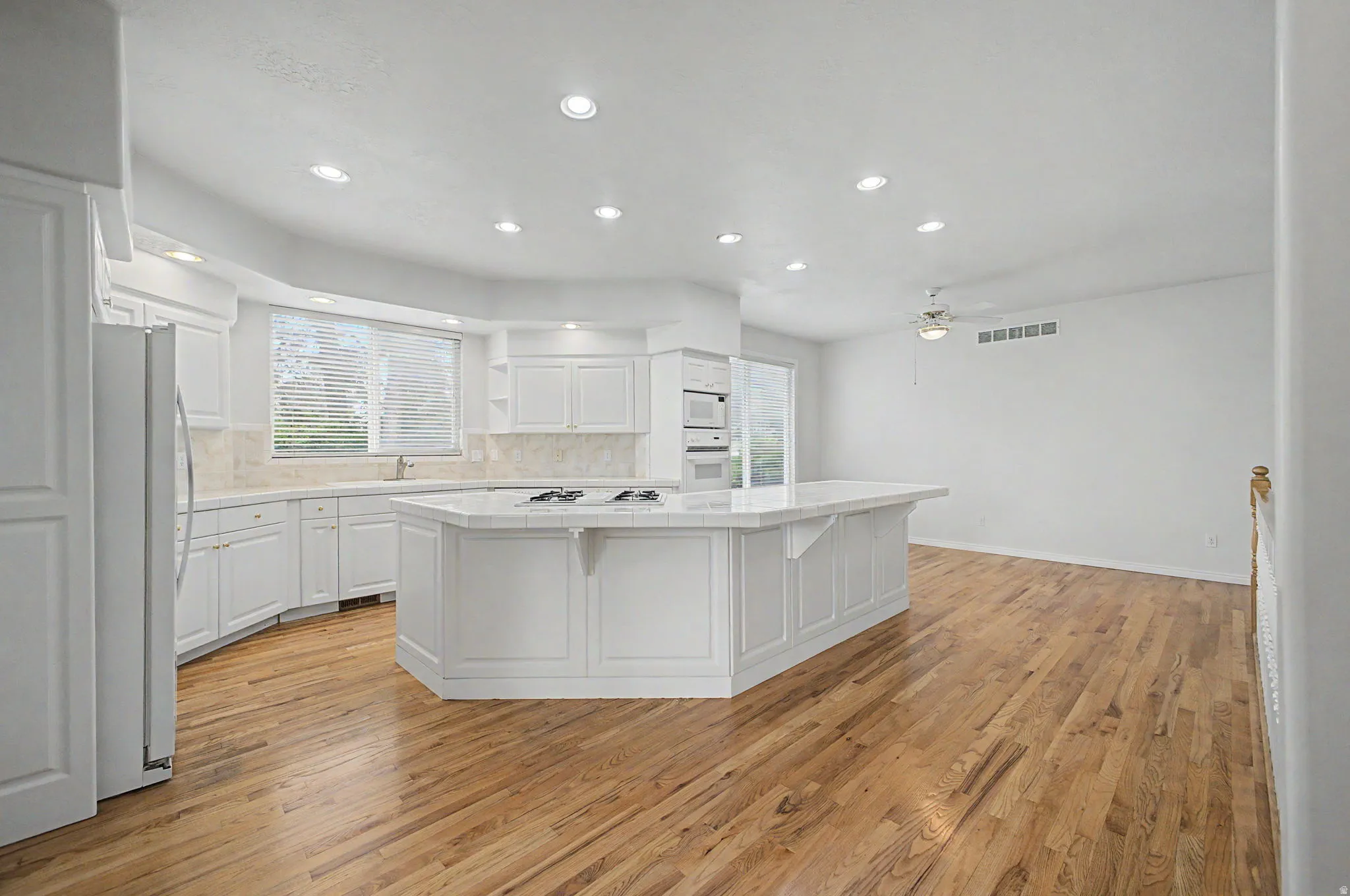 Kitchen featuring a large central island with a cooktop, built-in double ovens, recessed lighting, wood-finish flooring, and white cabinetry