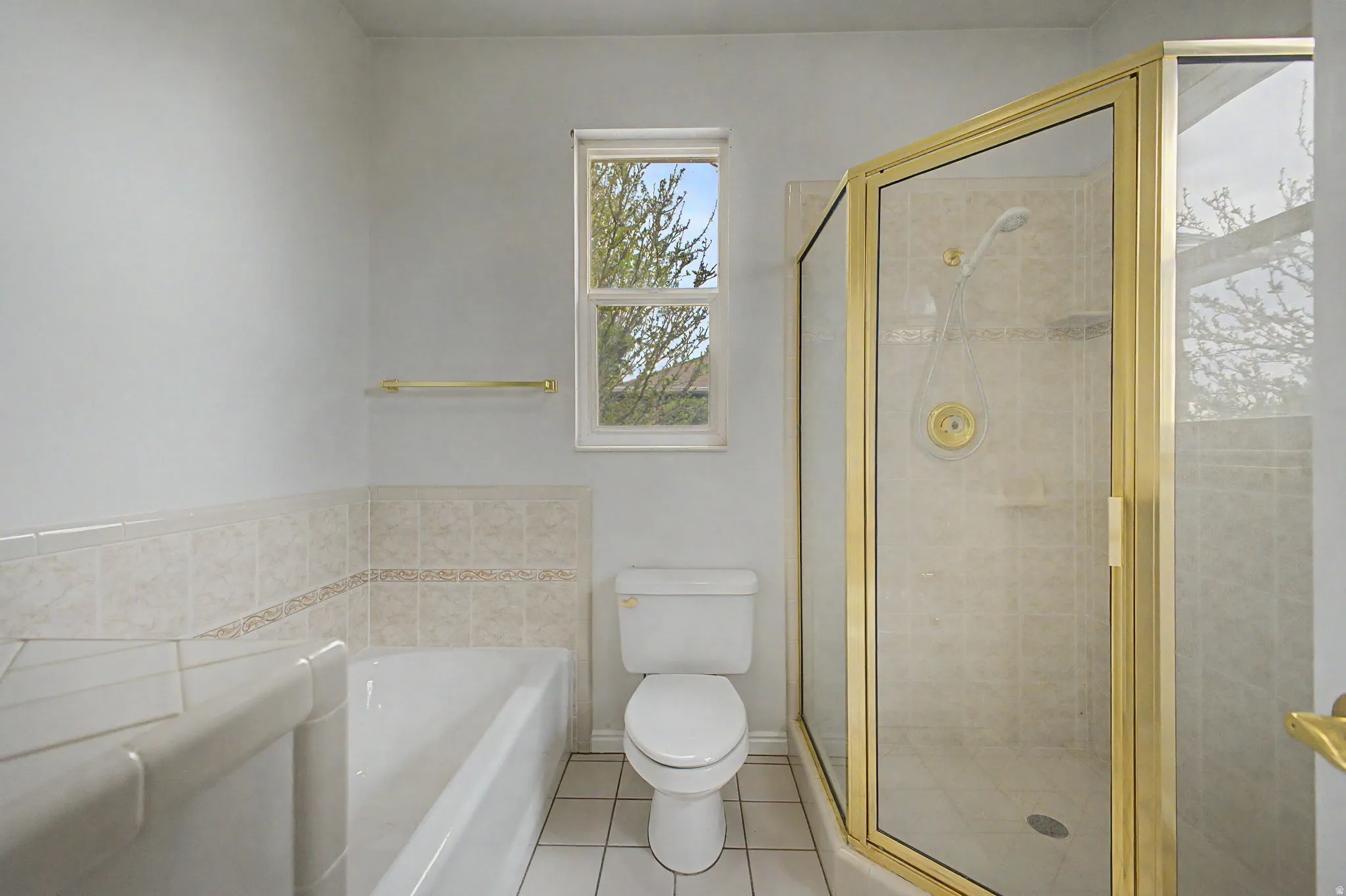 Bathroom featuring a gold-framed glass shower enclosure, a built-in bathtub, and a window