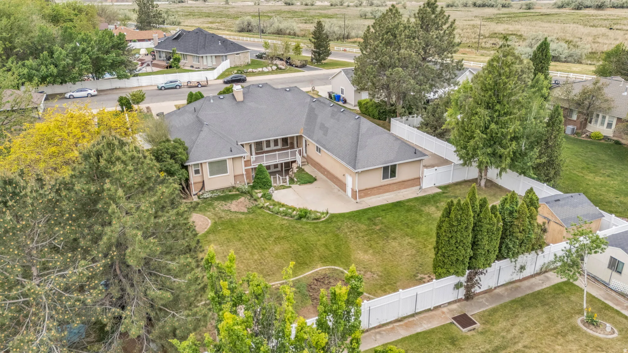 Spacious residential property featuring a large backyard with manicured lawn, multi-level patio, mature trees, and a full privacy fence