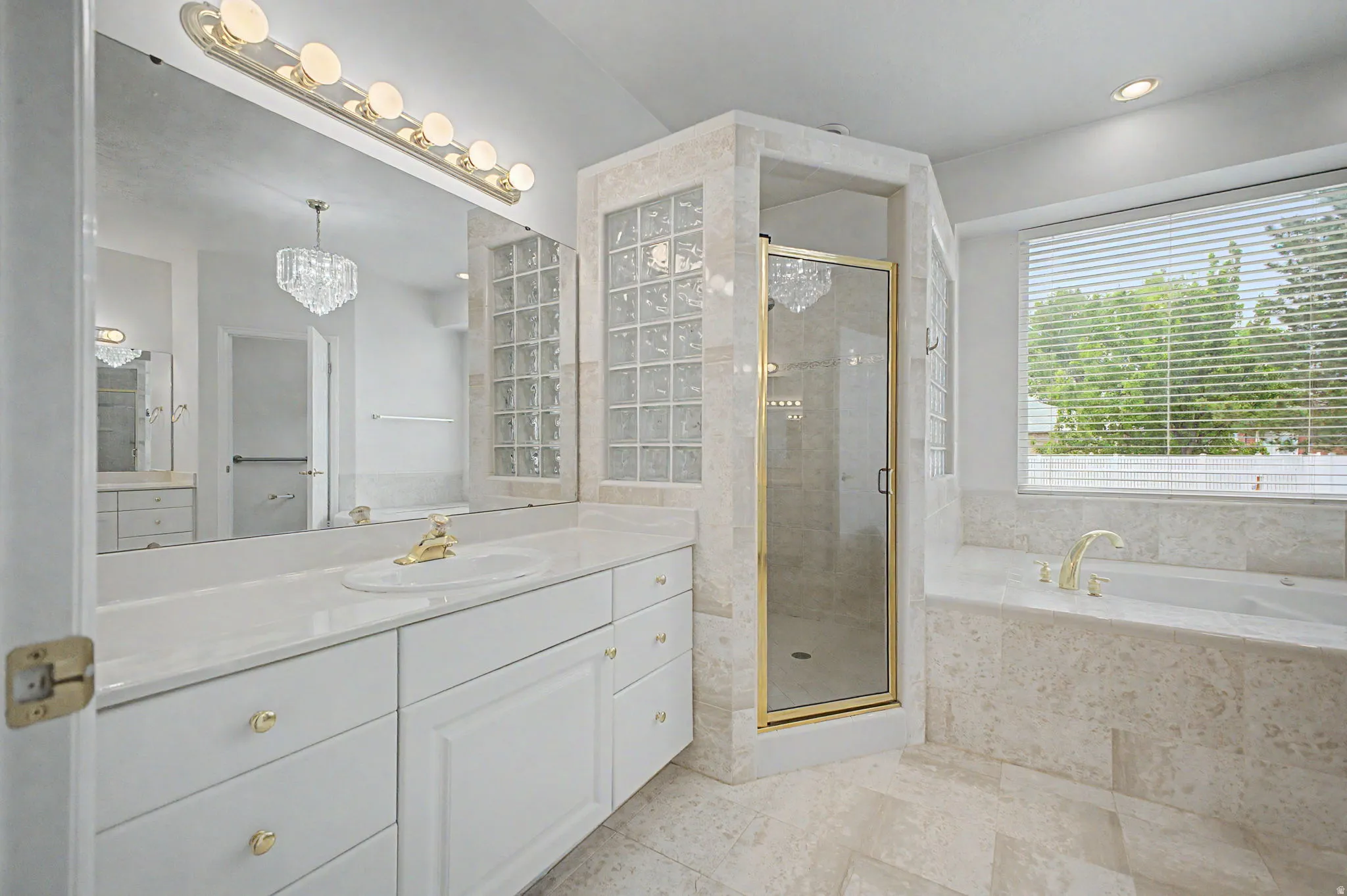 Bathroom featuring a double vanity with white cabinetry, a built-in tub, a glass-enclosed shower, and a large window