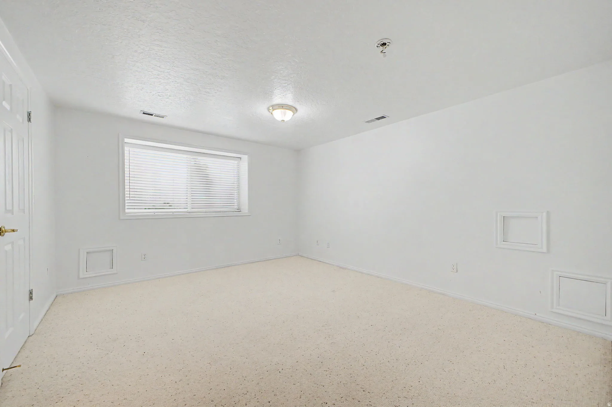 Spacious room featuring neutral carpeting, white walls, and a window with horizontal blinds