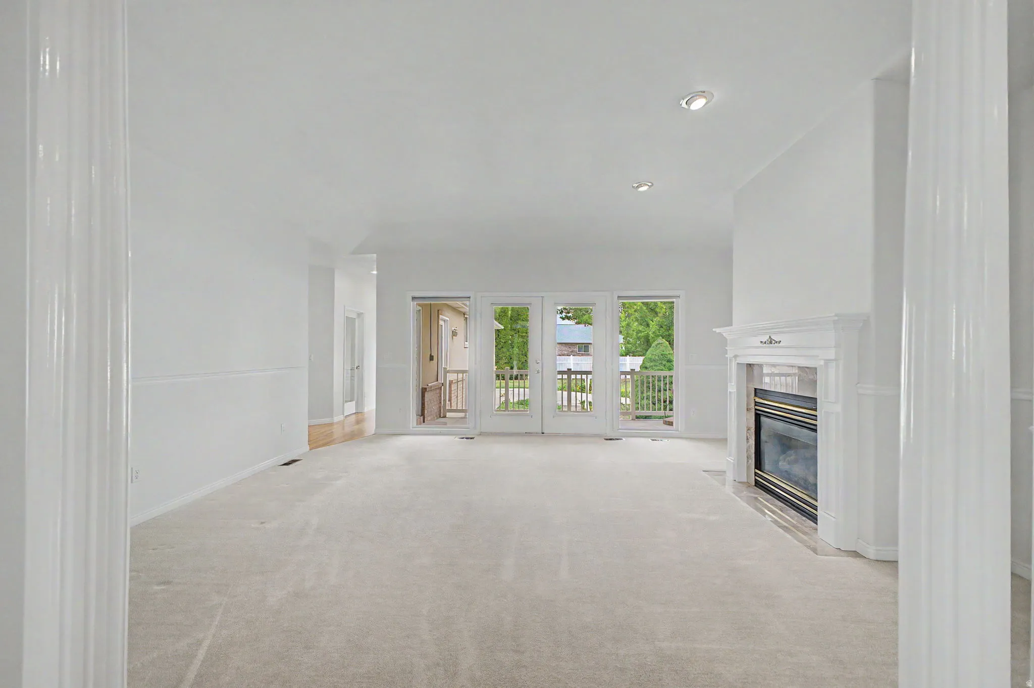 Spacious living area featuring light-colored carpeting, a white mantel fireplace, and recessed lighting
