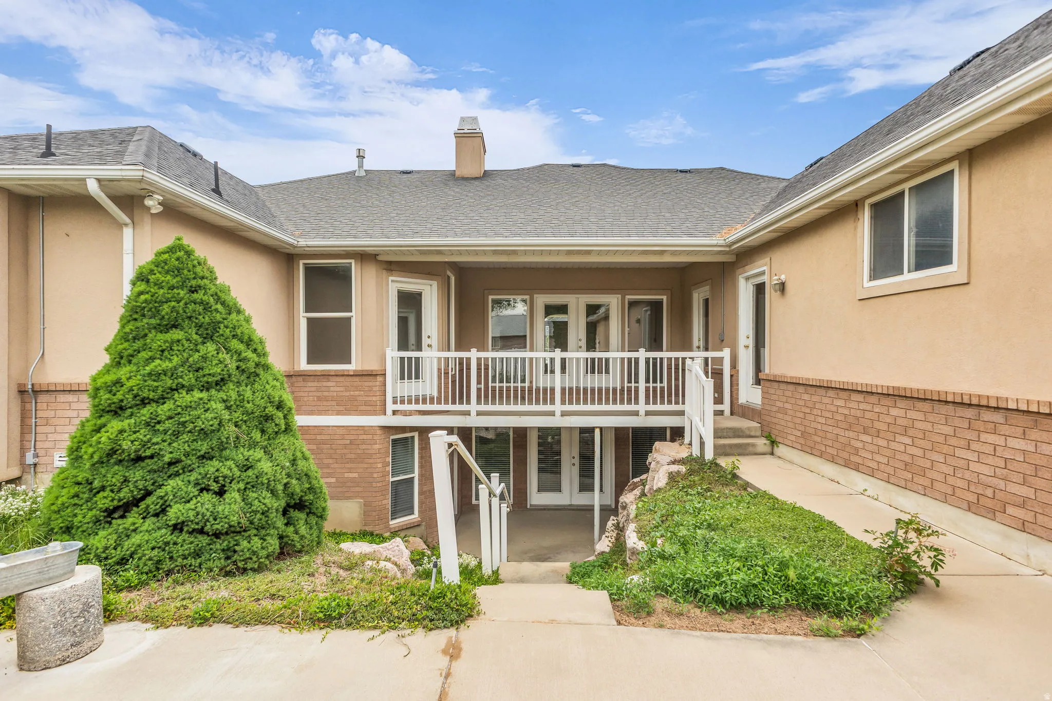 Multi-level exterior featuring stucco and brick finishes, a covered second-story balcony with white railings, and a lower-level patio with double glass doors