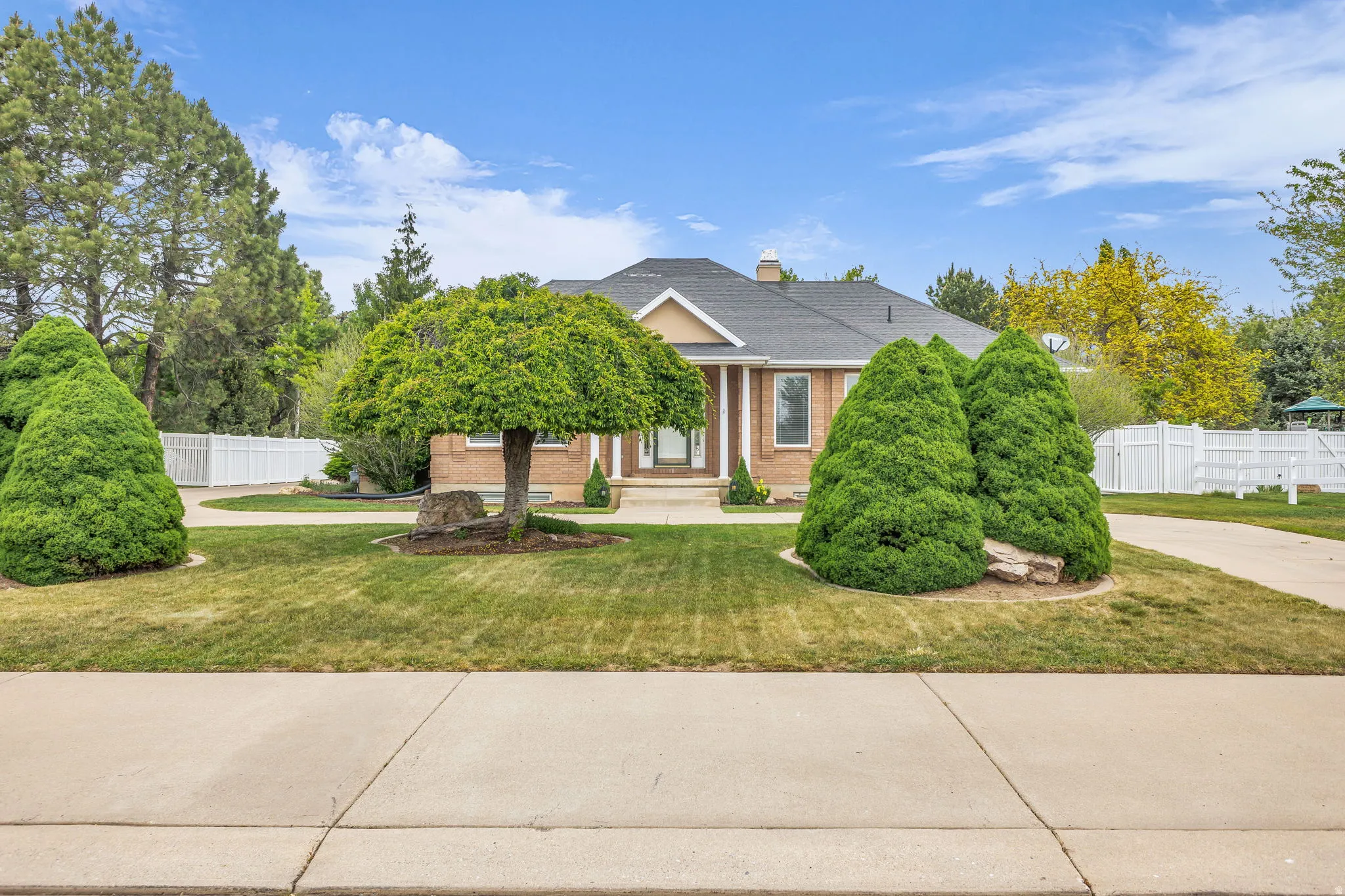 Brick-front residence featuring a covered entry, mature landscaping, and an expansive concrete driveway