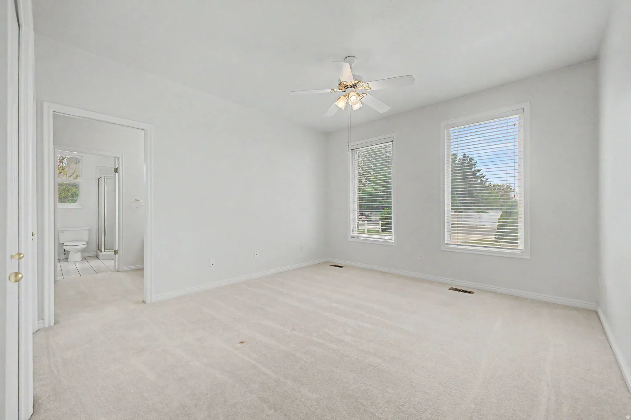 Carpeted room with white walls, two windows featuring horizontal blinds, and a ceiling fan with integrated lighting