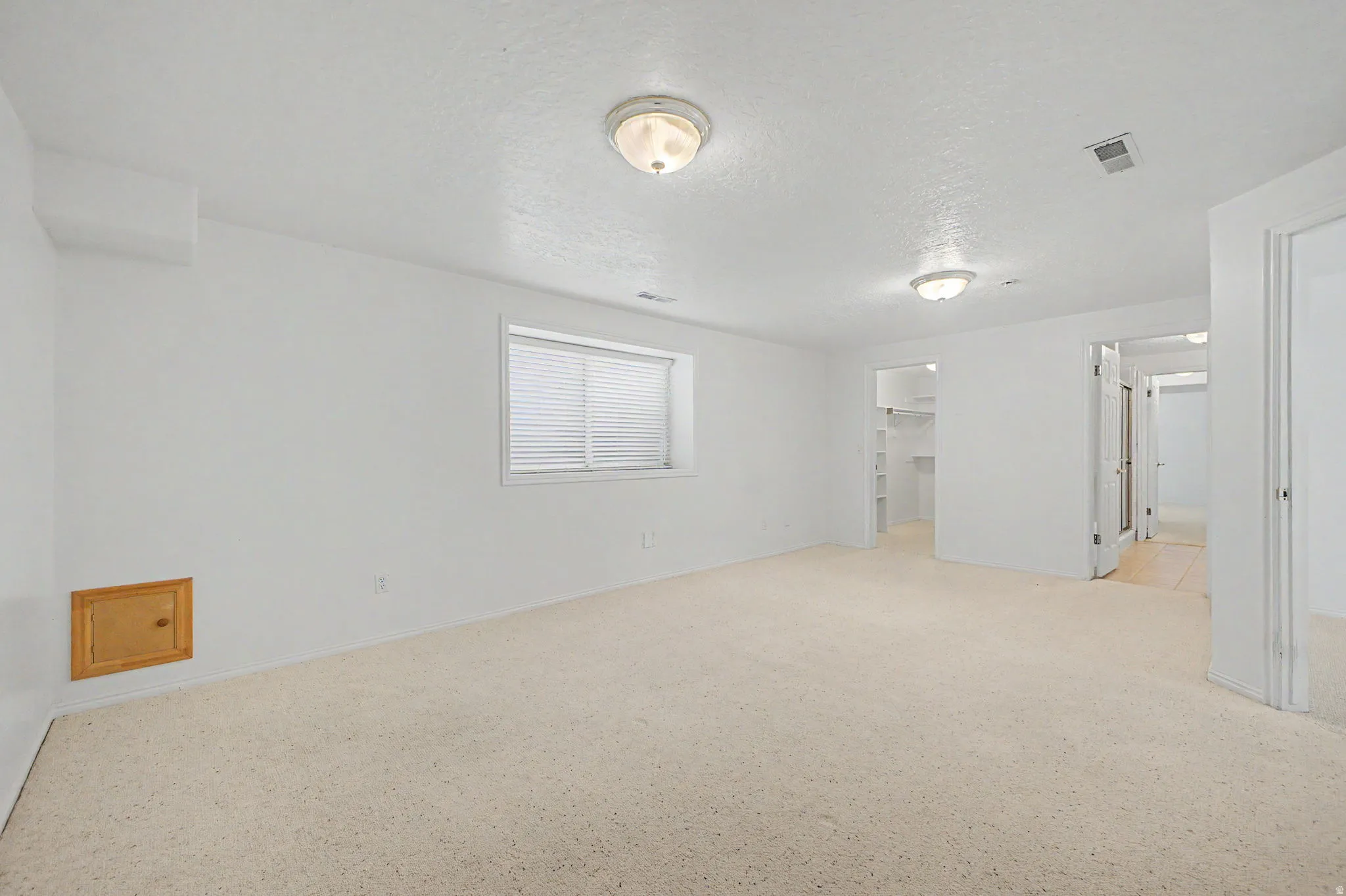 Spacious room featuring light-colored carpeting, white painted walls, and a window with horizontal blinds