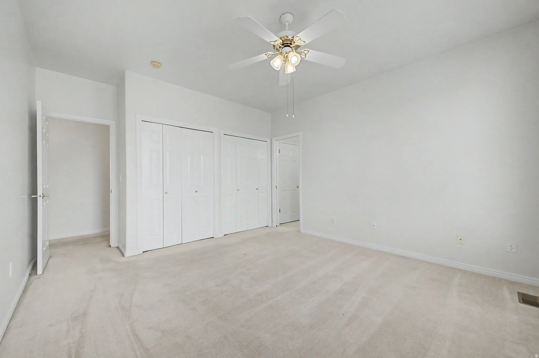 Spacious room featuring neutral carpeting, a ceiling fan with integrated lighting, and multiple bi-fold closet doors