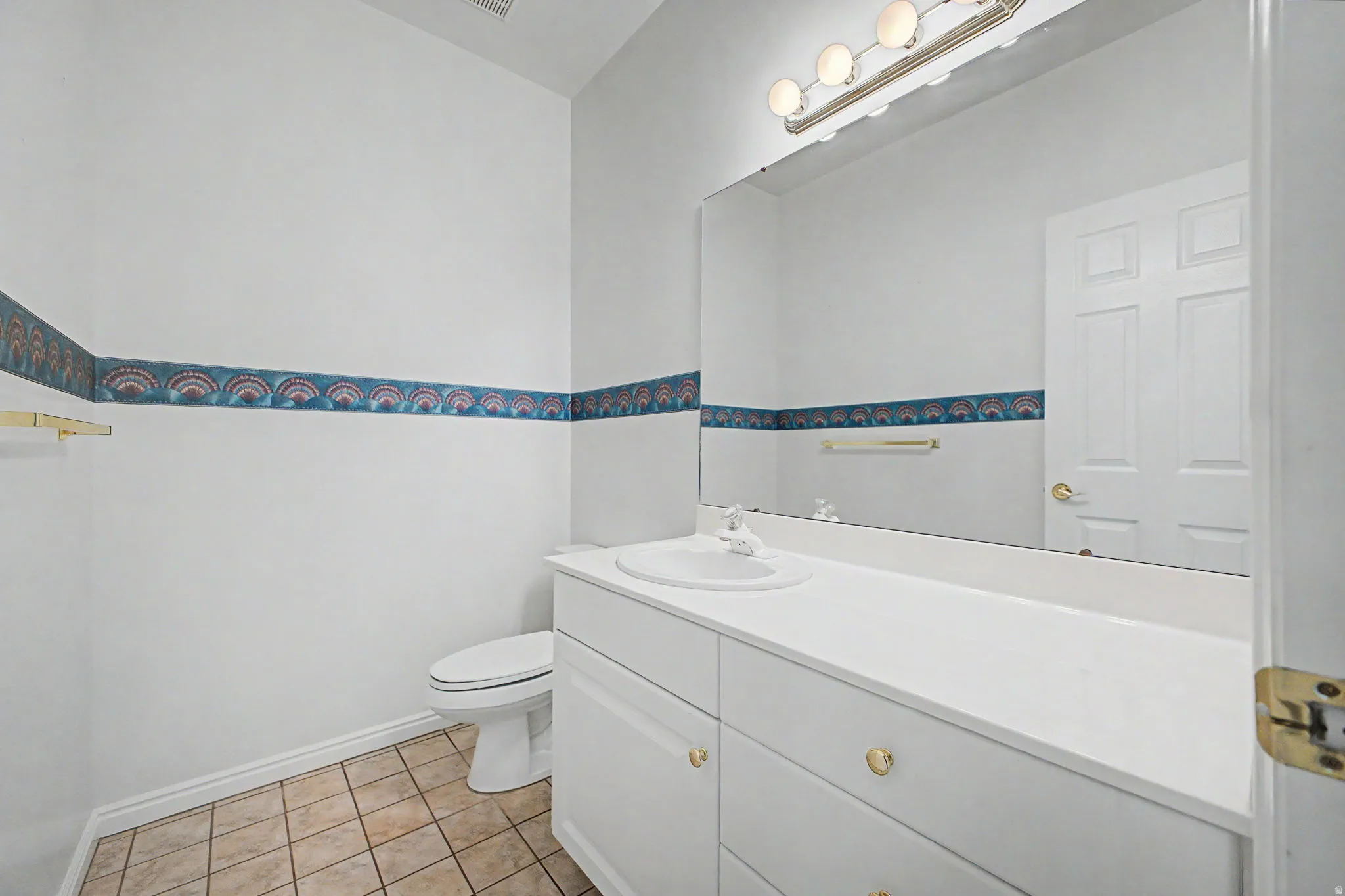 White vanity with integrated sink, brushed nickel lighting fixture, large wall-mounted mirror, and neutral tiled flooring