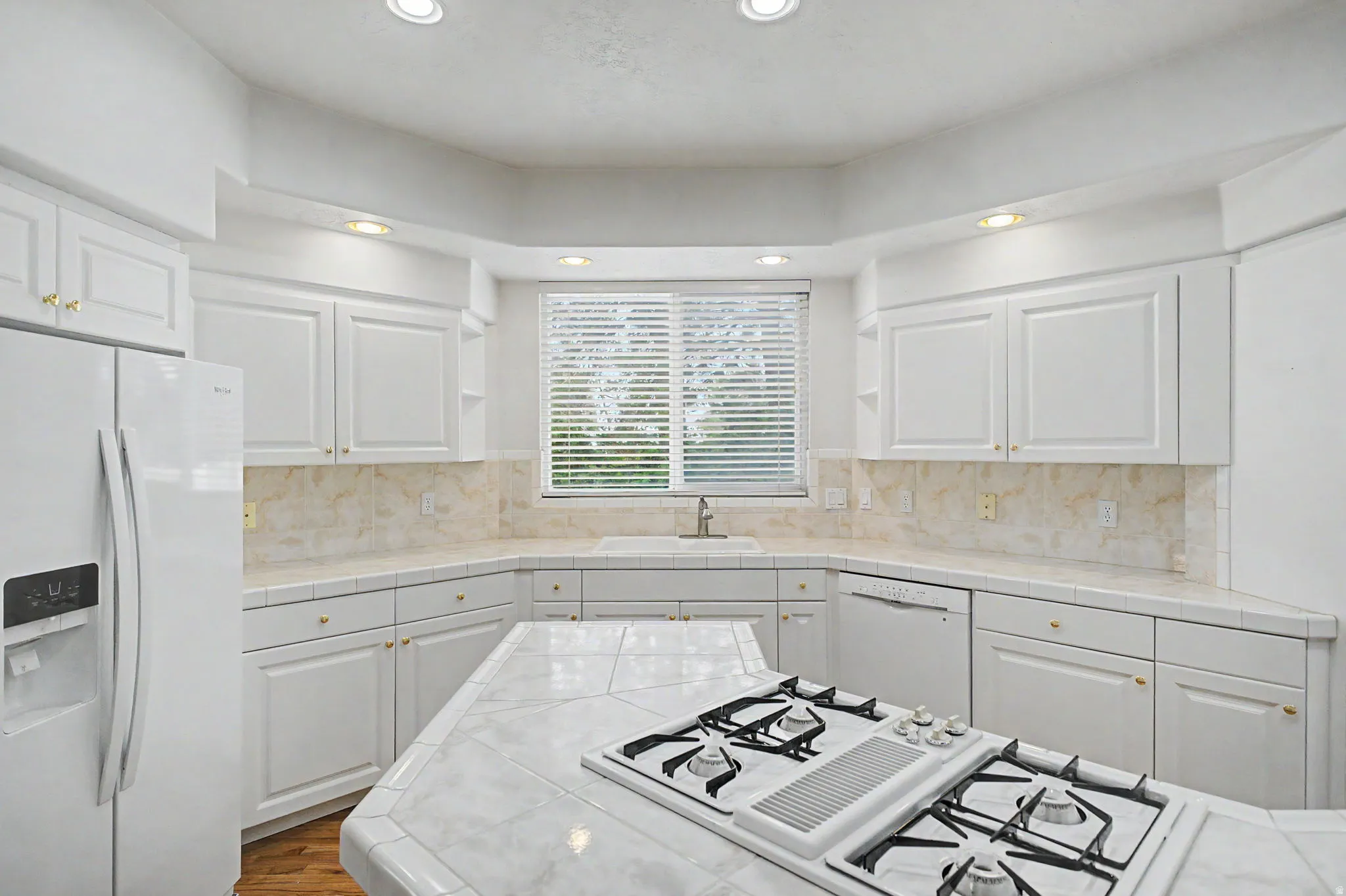 Kitchen featuring white cabinetry with gold-toned hardware, a tile countertop, and a built-in gas range on the island