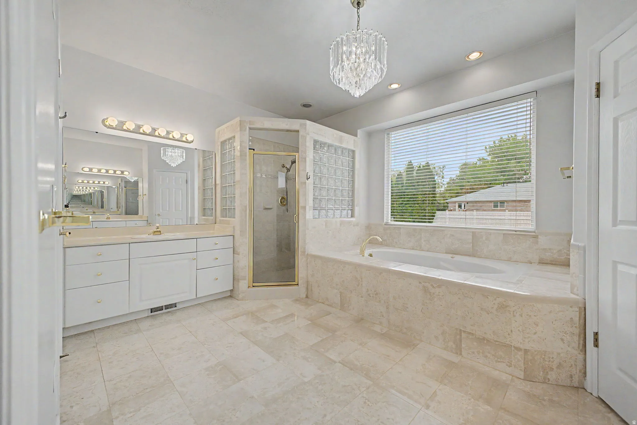 Spacious bathroom featuring a large soaking tub with a tiled surround, a separate glass-enclosed shower, dual vanity with white cabinetry, and recessed lighting