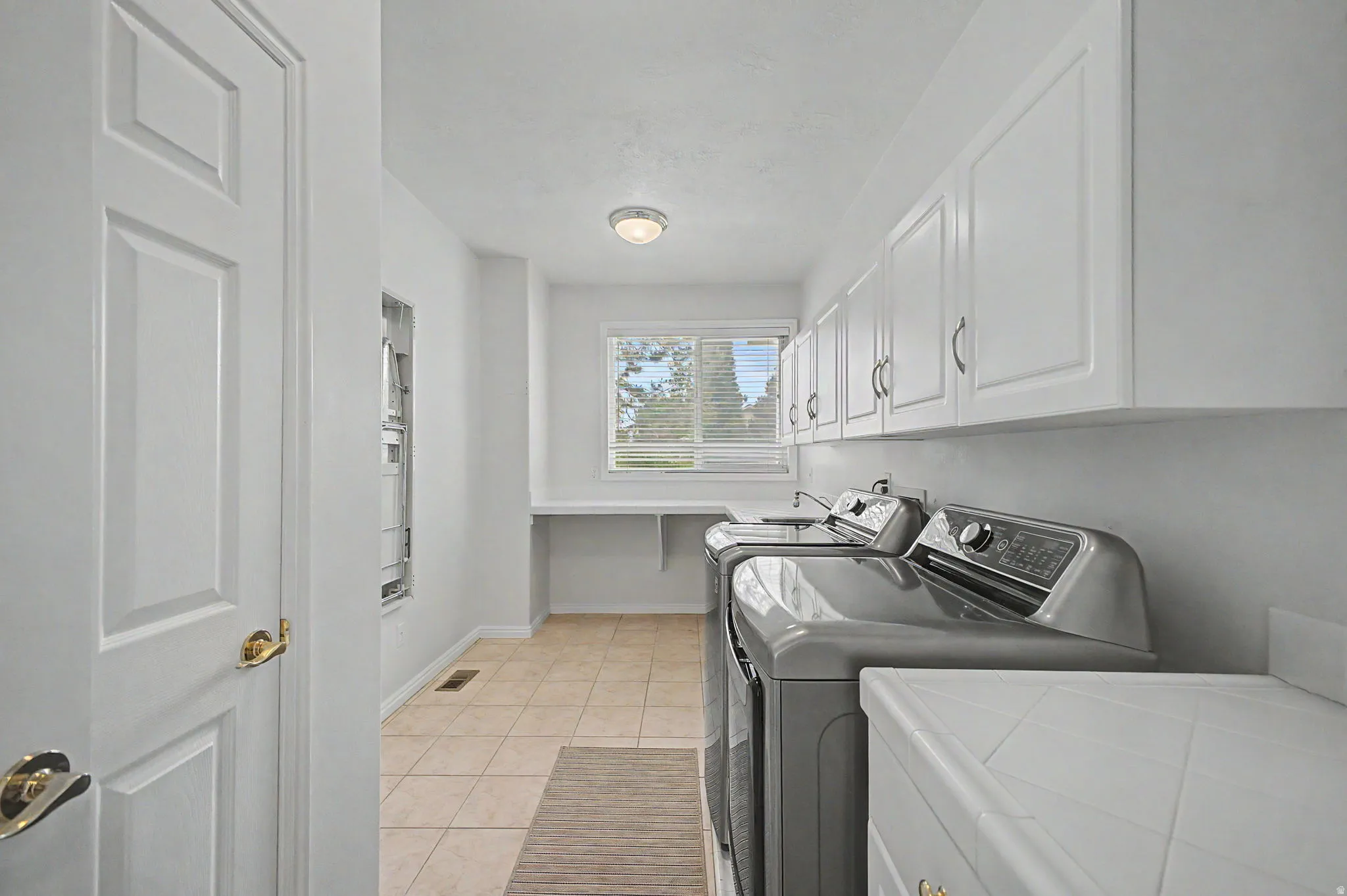 Dedicated laundry room featuring tile flooring, white shaker-style cabinetry, and a countertop workspace