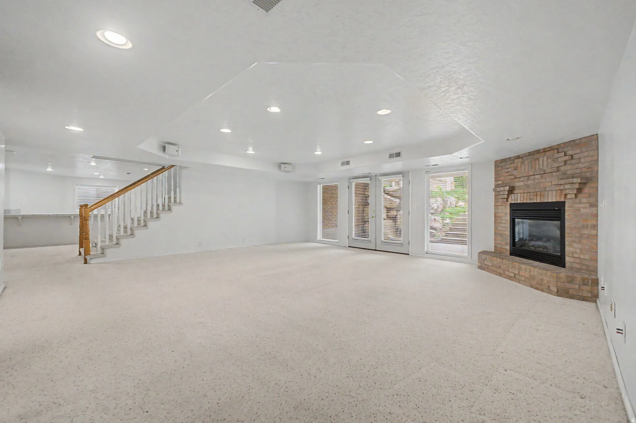 Spacious room featuring light-toned carpeting, a brick fireplace, and double glass doors