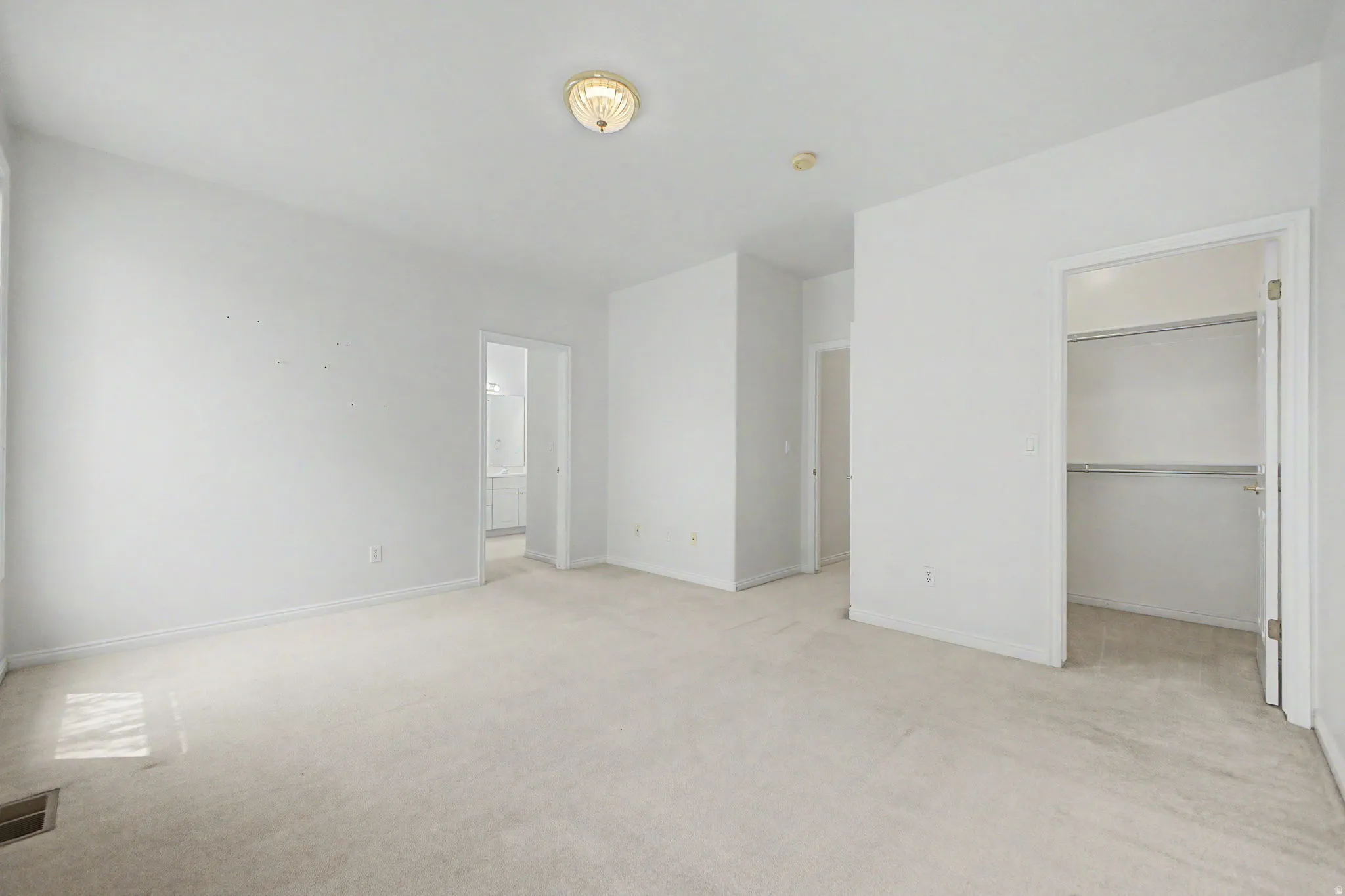 Spacious room featuring neutral carpet flooring, white painted walls, a flush-mount ceiling light, and an open closet with shelving and hanging rods