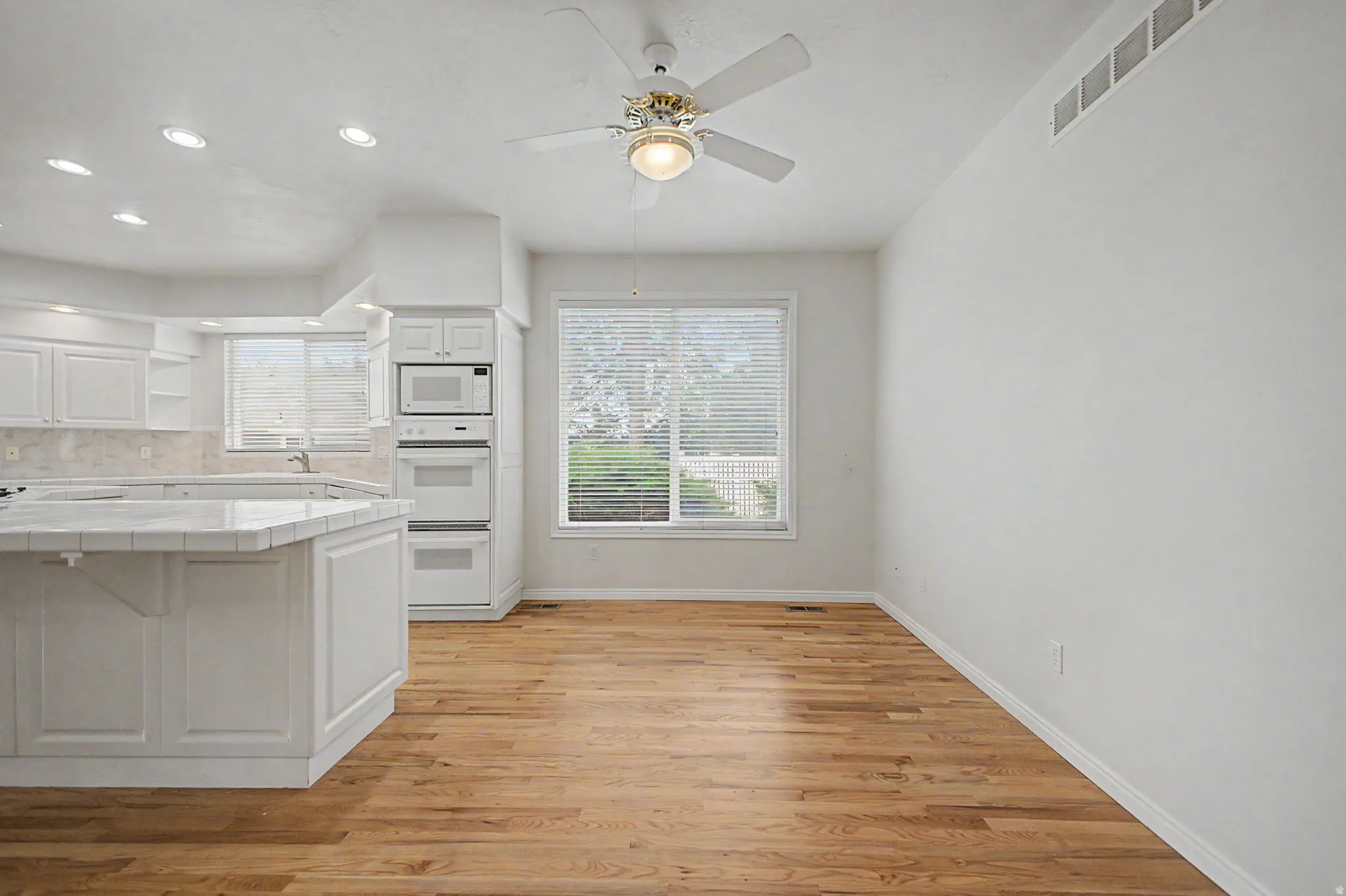 Kitchen and dining area featuring wood-finish flooring, white cabinetry, built-in double ovens, and a tile countertop
