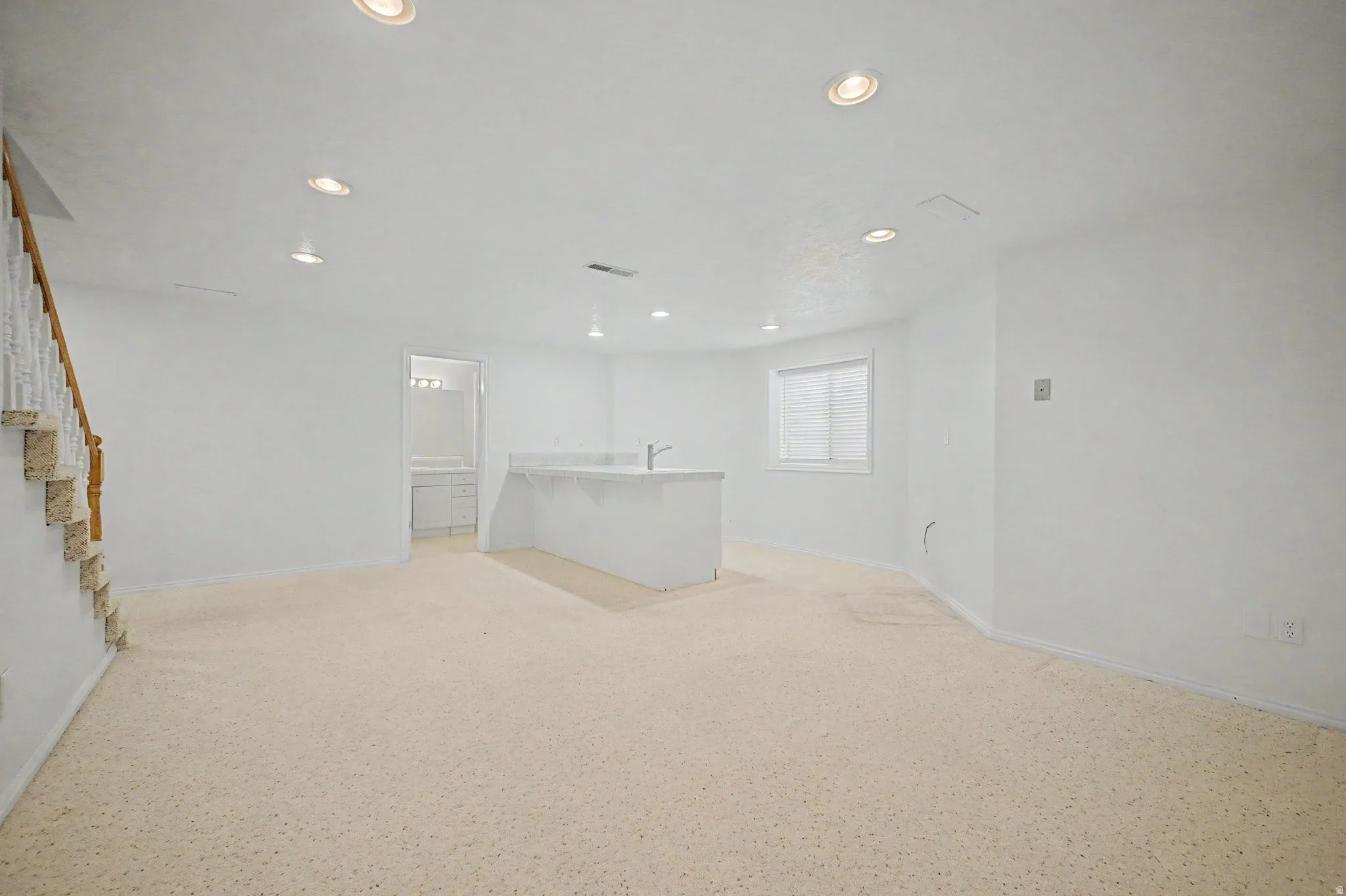 Spacious room featuring light-colored carpeting, recessed lighting, and a built-in wet bar with a sink and countertop