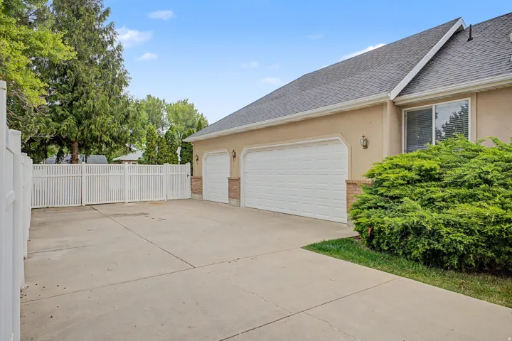 Expansive concrete driveway with a two-car garage featuring individual white doors and brick accents