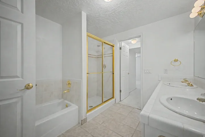 Bathroom featuring a dual vanity, gold-framed glass shower enclosure, and a built-in bathtub with tiled surround