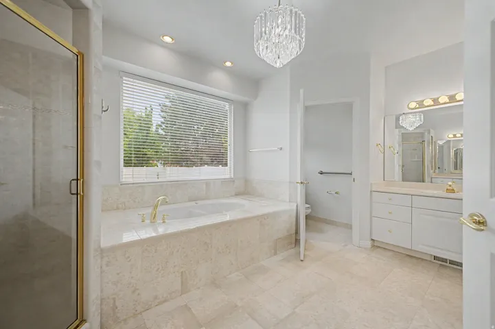 Spacious bathroom featuring a built-in soaking tub with gold-finish fixtures, a separate glass-enclosed shower with gold-finish trim, and a double vanity with a large mirror