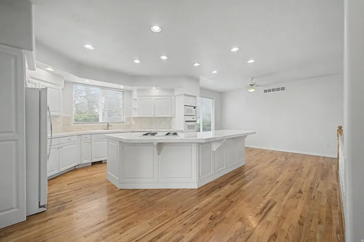 Kitchen featuring a large central island with a cooktop, built-in double ovens, recessed lighting, wood-finish flooring, and white cabinetry