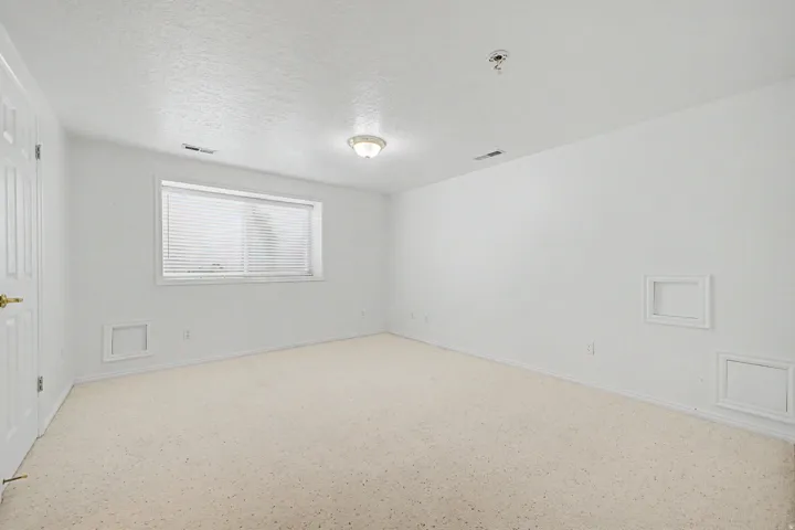 Spacious room featuring neutral carpeting, white walls, and a window with horizontal blinds