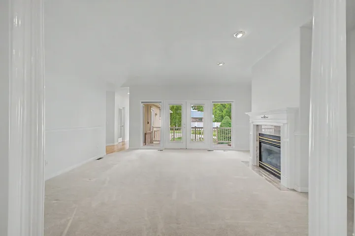 Spacious living area featuring light-colored carpeting, a white mantel fireplace, and recessed lighting