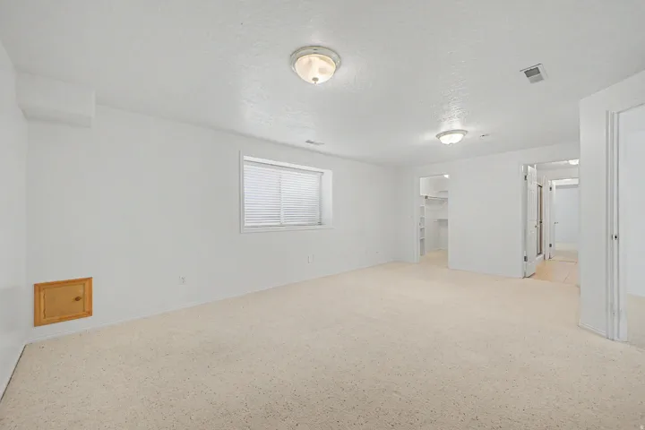 Spacious room featuring light-colored carpeting, white painted walls, and a window with horizontal blinds
