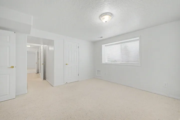 Bright room featuring light-colored carpeting, a window with blinds, and multiple white paneled doors with brass-finish hardware