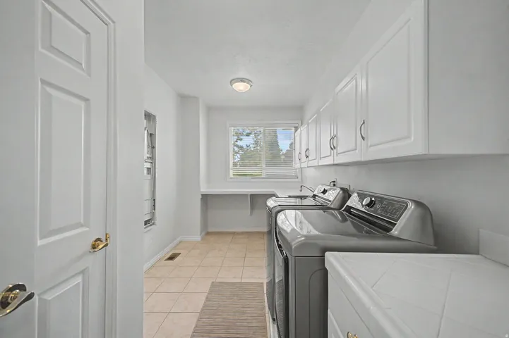 Dedicated laundry room featuring tile flooring, white shaker-style cabinetry, and a countertop workspace