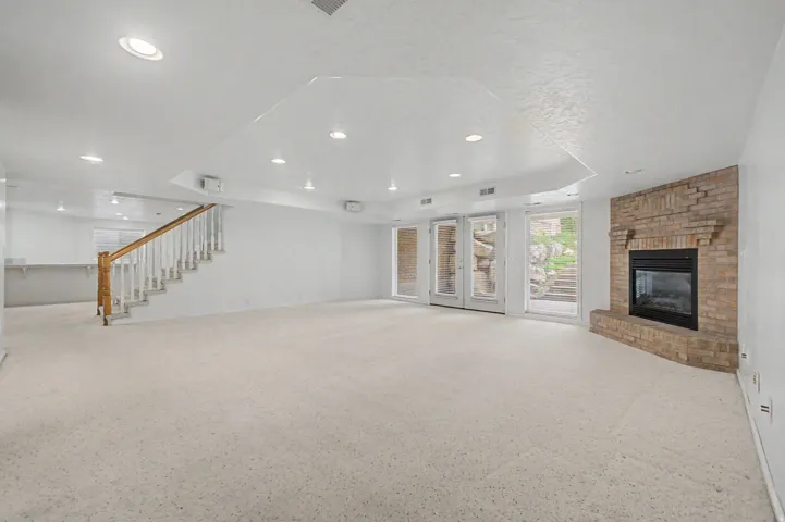 Spacious room featuring light-toned carpeting, a brick fireplace, and double glass doors