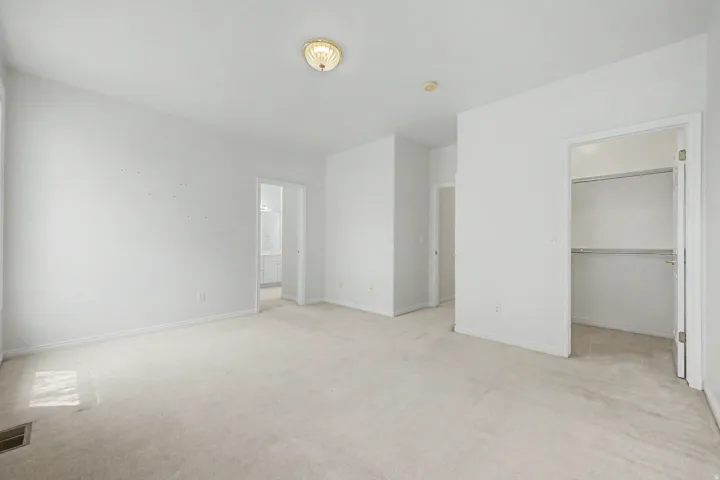Spacious room featuring neutral carpet flooring, white painted walls, a flush-mount ceiling light, and an open closet with shelving and hanging rods