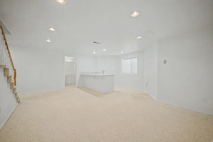 Spacious room featuring light-colored carpeting, recessed lighting, and a built-in wet bar with a sink and countertop