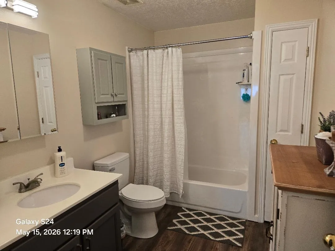 Bathroom featuring a vanity with a white countertop, dark wood-finish cabinetry, a built-in medicine cabinet, a full-size bathtub with shower, and wood-finish flooring