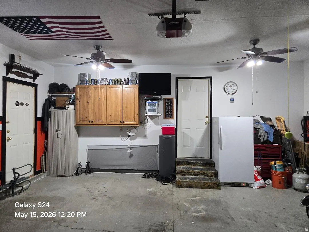 Garage space featuring two ceiling fans with integrated lighting, wood-finish wall cabinetry, and multiple entry doors