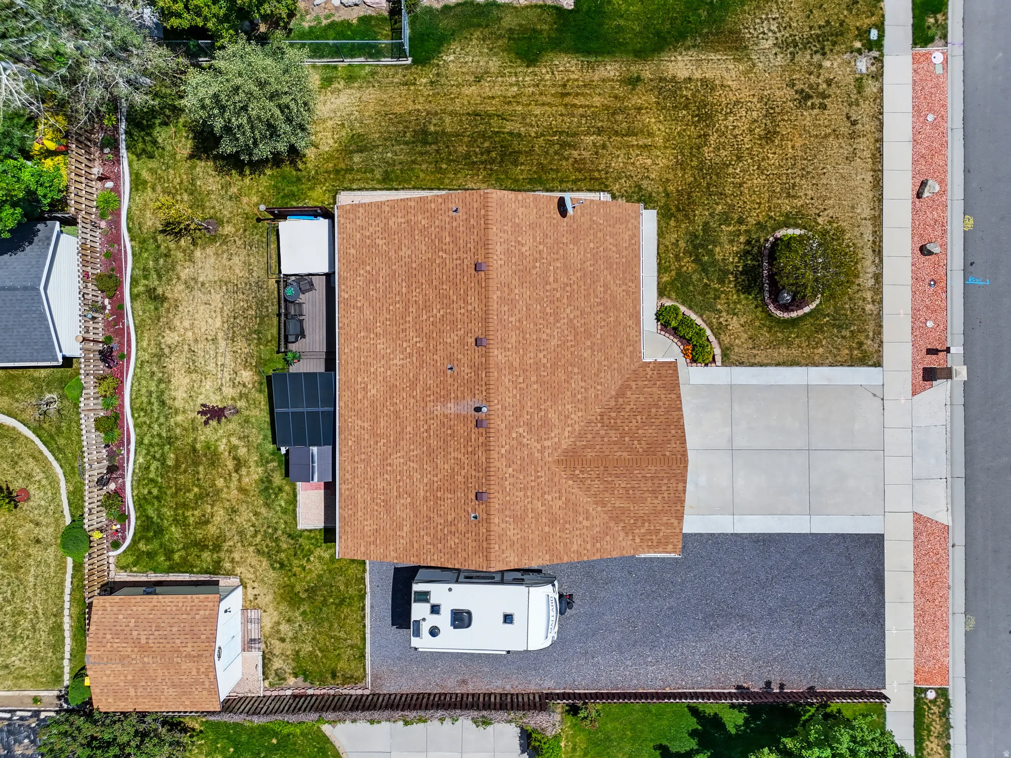 Property featuring a brown shingle roof, concrete driveway, and a gravel parking area