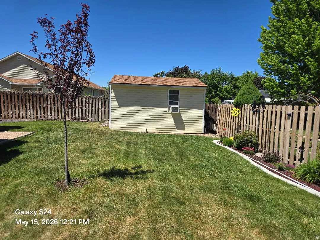 Expansive backyard featuring a manicured lawn, a detached storage shed/workshop with a window and air conditioning unit, a young deciduous tree, and a wooden privacy fence