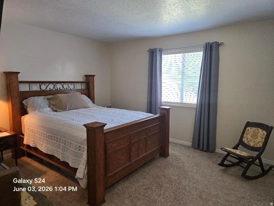 Carpeted room with a large window featuring blinds and grey curtains