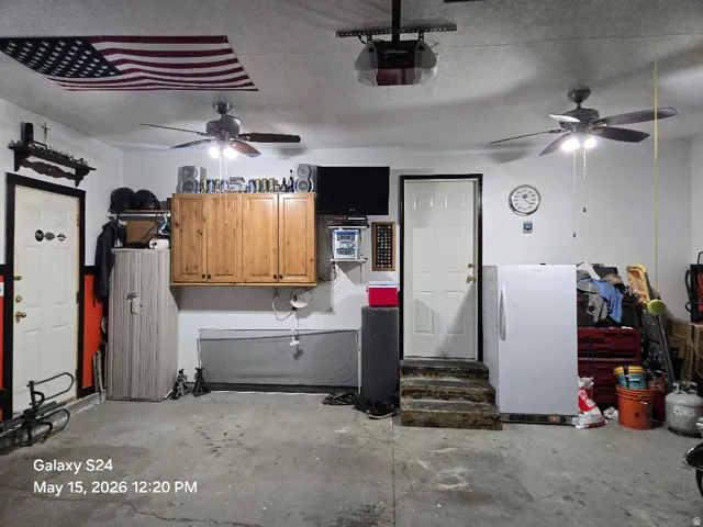 Garage space featuring two ceiling fans with integrated lighting, wood-finish wall cabinetry, and multiple entry doors