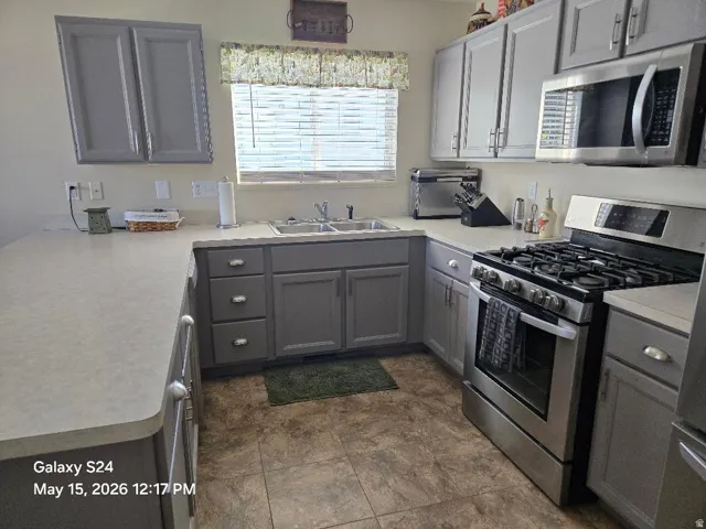 Kitchen featuring L-shaped countertops, gray cabinetry, stainless steel appliances, and a gas range