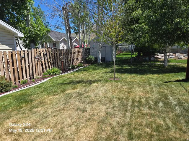 Expansive grassy yard featuring mature trees, a wooden privacy fence, and defined landscaping beds with mulch