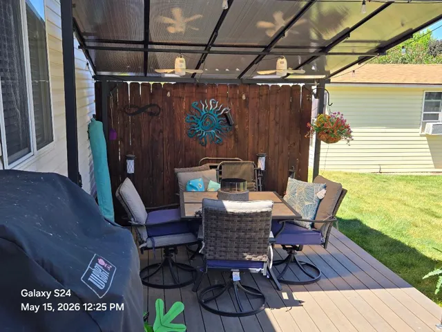 Expansive outdoor living area featuring a composite deck, a slatted wood privacy fence, and a clear panel patio cover with integrated ceiling fans and string lighting
