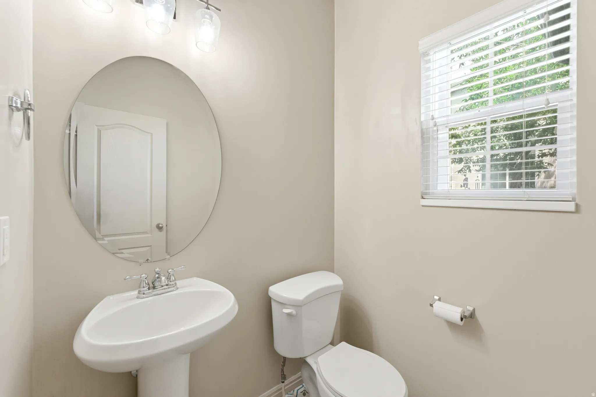 Pedestal sink with chrome faucet, oval mirror, and three-light vanity fixture